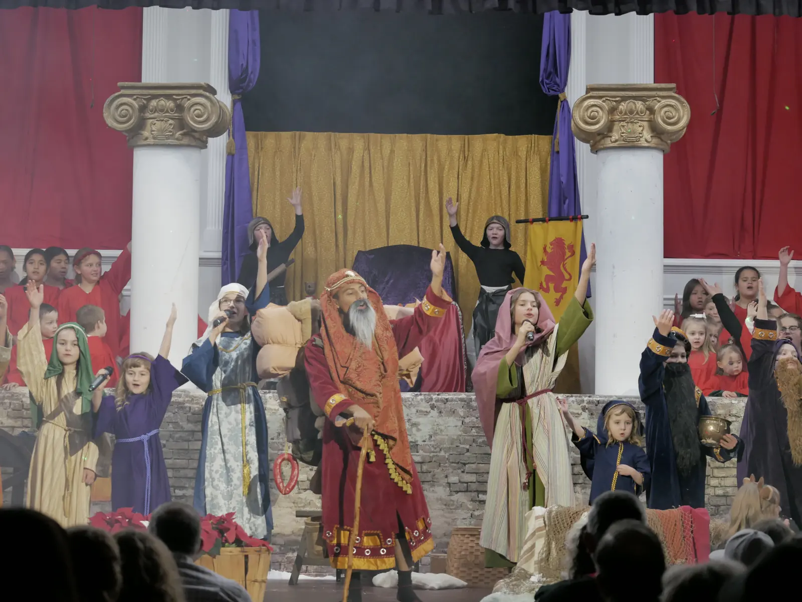The whole cast singing with hands raised before the gold-curtained throne