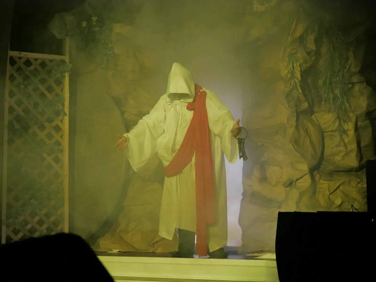 A hooded figure in white with a red sash and a ring of keys at the open tomb