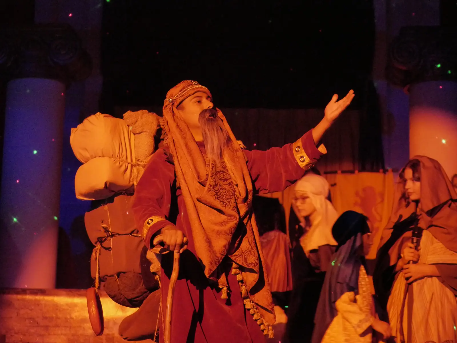 The fourth wise man, in a red robe with his pack and staff, reaching upward